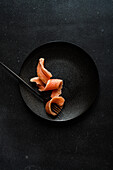 Top view of healthy salmon slice served on black plate near fork against dark surface