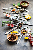 Variety of spices and seeds, including sunflower seeds, anise stars, and rosemary, artfully arranged in spoons on a textured surface with lemon slices adding a fresh touch