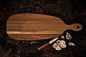 Top view of wooden oval shaped cutting board placed near knife and garlic on rough surface