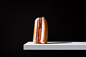 Appetizing bun with sausage and ketchup placed on white wooden board against black background in studio