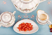 A vintage porcelain tea set displayed with goji berries on a plate, the setup on a pastel blue background.