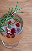 A rosemary-infused winter cocktail garnished with fresh cranberries and sprigs, served in a tall glass on a wooden surface.