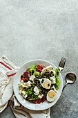 Draufsicht auf einen Teller mit Keto-Salat mit Salatblättern, gekochten Eiern, Kapern, Tomaten, roten Zwiebeln und Blumenkohlgemüse auf dem Tisch zwischen Serviette und Besteck