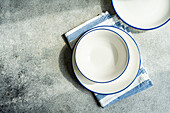 Top view of minimalistic rustic table setting with white plates and striped napkin on gray surface in daylight
