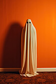 Frontansicht eines Gespenstes, das in der Halloween-Nacht vor einer orangefarbenen Wand steht, erstellt mit generativer KI-Technologie