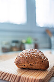 A seed-encrusted artisan bread loaf on a pine wood cutting board, with a blurred kitchen background