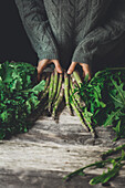 Unrecognizable person in gray sweater standing at wooden table with fresh asparagus stems