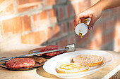 Anonymous person pours olive oil on burger buns beside raw patties