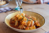 Freshly cooked pasta with fork served in plate on wooden table at restaurant