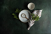 Top view of table decoration with fresh pistachio plant placed near bowls with spoon and napkin against dark gray surface