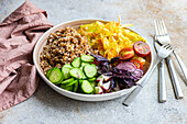 High angle of bowl with delicious buckwheat containing sliced fresh basil plant with cabbage and cucumber with cutlery placed on gray table with napkin