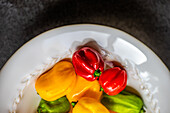 Top view of different colored peppers placed in a round white ceramic plate on a concrete background