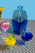 Von oben Glasgefäß mit blauer Farbe Cocktail und Sorten von bunten Getränken Long Island Iced Tea Wein Daiquiri Lemon Drop Getränk auf gestreiften Oberfläche im Licht platziert
