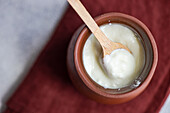 Top view of traditional serving of Georgian sour yogurt known as Matsoni in clay pot with wooden spoon on brown napkin against blurred background