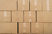 Strukturierter Hintergrund von Reihen von Kartonbehältern mit Klebebändern auf beiger Oberfläche in einem Lagerhaus