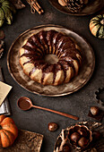 From above tasty appetizing pumpkin cake with chocolate cream on table decorated with autumn vegetables