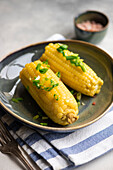 From above of boiled corn with salt and green onion served on plate on grey background