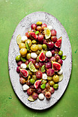 From above fresh ripe grapes, olives, figs and mozzarella seasonal christmas salad placed on plate on green tabletop background