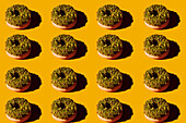 Von oben viele Donuts mit grünem Belag und Nüssen auf gelbem Hintergrund