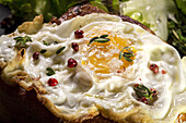 Fried egg on brioche served on tray with fresh lettuce for appetizing breakfast on black background