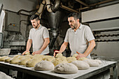 Älterer bärtiger ethnischer Bäcker formt Brot aus Teig am Tisch mit Mehl und Schüssel in einer Bäckerei