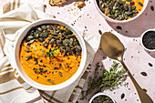 Top view of appetizing homemade pumpkin purees with seeds and herbs in bowls placed on table near crispy bread slices in kitchen