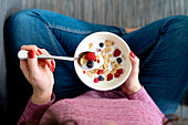 Top view of crop unrecognizable female with bowl of cornflakes and ripe berries with milk for breakfast in light room
