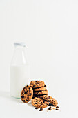 Ein Haufen süßer, knuspriger Kekse mit Schokoladenstückchen liegt auf einem Tisch mit Krümeln und Milch auf weißem Hintergrund in einem Zimmer