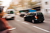 Unscharfe Autos und Busse fahren auf einer asphaltierten Straße neben einem nicht erkennbaren Fußgänger in einer herbstlichen Stadt