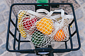 Umweltfreundlicher Netzbeutel mit frischem Obst und Gemüse im Metallkorb eines geparkten Fahrrads in der Stadt (von oben)