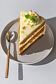 From above slice of tasty sweet carrot sponge cake with cream decorated with mint leaf served on plate with spoon on table in light room on the background
