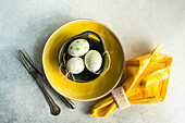 From above place setting for Easter dinner with yellow ceramic plate and bowl with easter eggs on concrete background