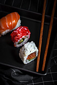 Top view composition of delicious fresh various sushi and bamboo chopsticks served on black platter on checkered cloth