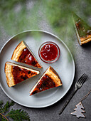 From above of plate with sliced delicious homemade cheesecake and jar with sweet jam placed on gray table