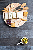 Draufsicht auf appetitlichen Käse, serviert auf einem Holztisch mit reifen Trauben und Crackern, dekoriert mit Rosmarinzweigen neben Oliven in Schalen auf dem Tisch