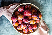 Fresh organic and ripe plum fruits in the bowl on concrete background