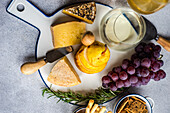 White ceramic cutting board with different kinds of cheese, ripe grape and pear with glass of white wine