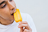 Crop happy male eating sweet orange ice lolly enjoying taste on white background