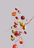 Strauß verschiedener frischer Früchte und Ingwer fällt in Glasflasche mit gesundem Saft vor grauem Hintergrund