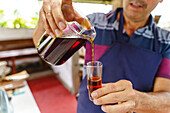 Unrecognizable crop male bartender pouring coffee from measuring container into transparent glass in house on blurred background