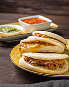 High angle of tasty Venezuelan arepas served on plate near bowls with sauces on table during lunch