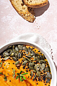 Top view of appetizing homemade pumpkin puree with seeds and herbs in bowl placed on table near crispy bread slices in kitchen