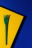 Overhead view of bright green eco friendly fork near yellow carton sheet on blue background