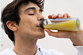 Carefree male drinking natural orange juice from bottle while enjoying taste with closed eyes
