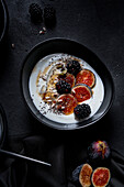 From above of appetizing healthy breakfast consisting of yogurt fresh figs and blackberries sprinkled with seeds and nuts placed on black table