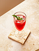 From above of tasty refreshing red beverage with ice cubes and aromatic mint leaves in glass on coaster