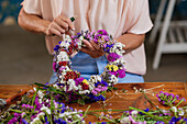 Crop anonymous female florist creating wreath from fresh colorful flowers while working at table in shop