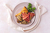 Top view of delicious croissants placed on plate with sprig of mint on pastel pink background