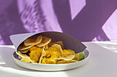 Appetizing fried chips and fish in paper wrapping served on plate on table with bright sunlight in cafe