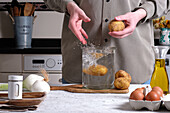 Crop anonymous person pouring raw unpeeled potatoes into jar with water while preparing ingredients for homemade Spanish omelette in kitchen